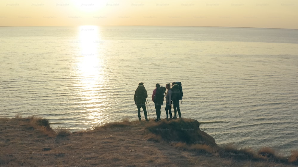 Los cuatro viajeros con mochilas parados en la orilla rocosa del mar