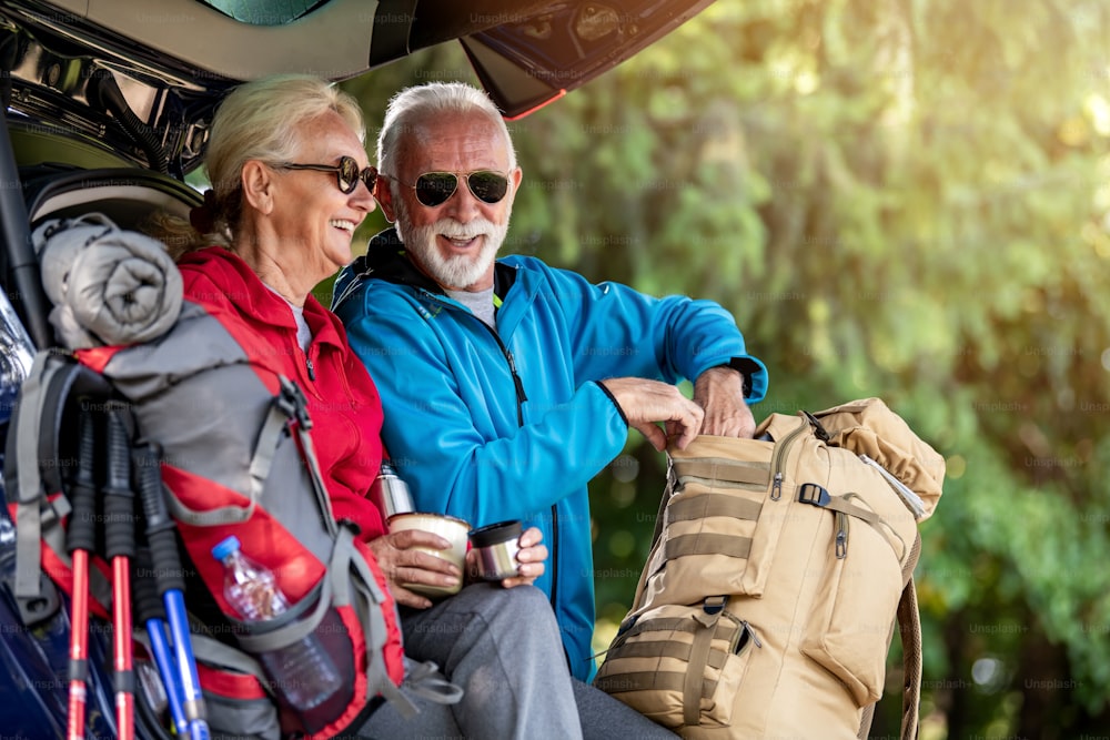 Hiking.Senior couple sitting in trunk and drink coffee while resting from hiking.