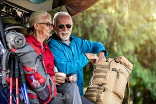 Hiking.Senior couple sitting in trunk and drink coffee while resting from hiking.