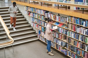 Jovens escolhendo livros e lendo-os na biblioteca