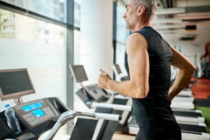 Mature athletic man running on treadmill during sports training in a gym.