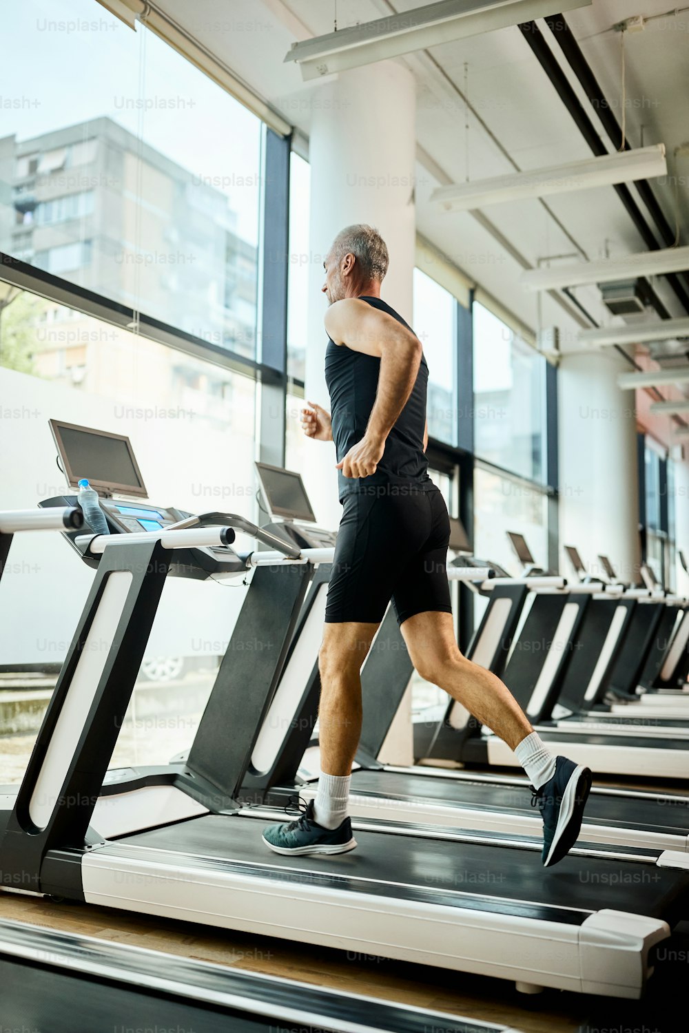 Niedrige Winkelansicht eines reifen Sportlers, der auf dem Laufband joggt, während er in einem Fitnessstudio trainiert.