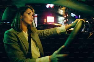 밤에 도시 거리를 통해 차를 운전하는 젊은 여자.