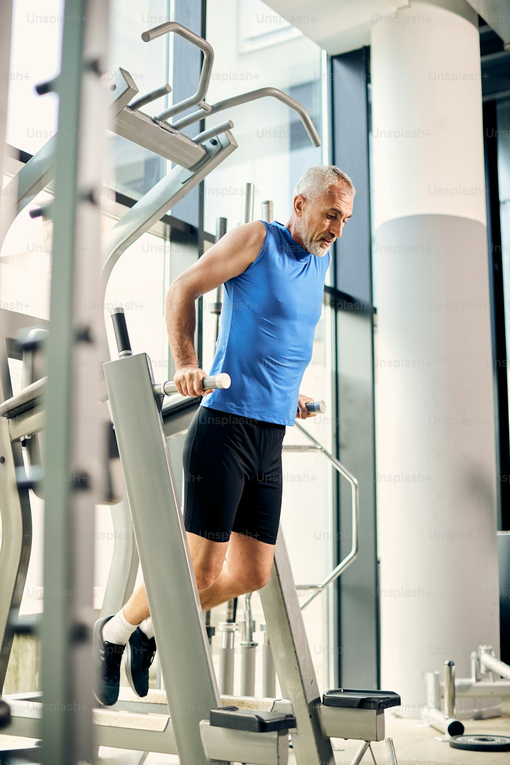 Mature athletic man practicing dips during sports training in a gym.