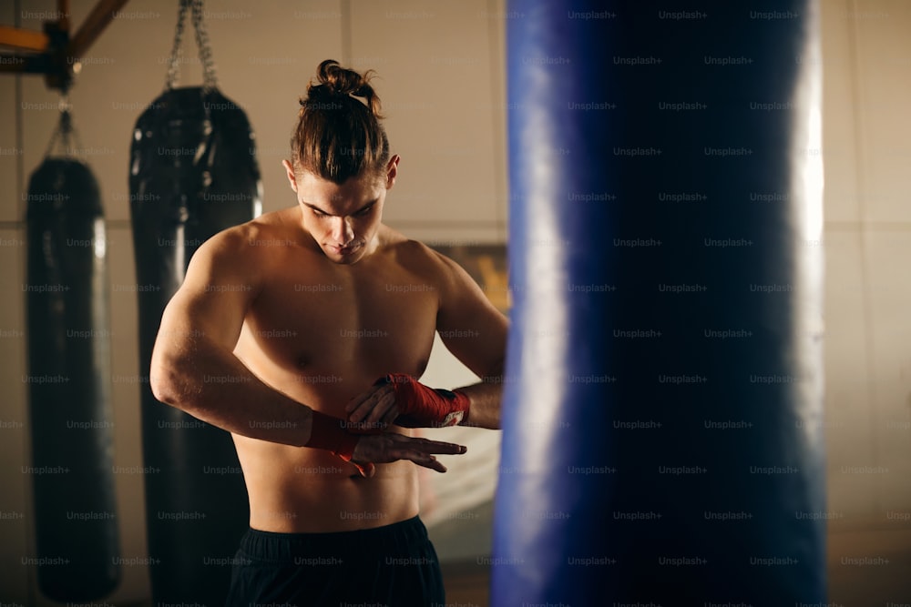 Un jeune boxeur panse les poings avec des lanières rouges avant de faire de l’exercice dans un club de santé.
