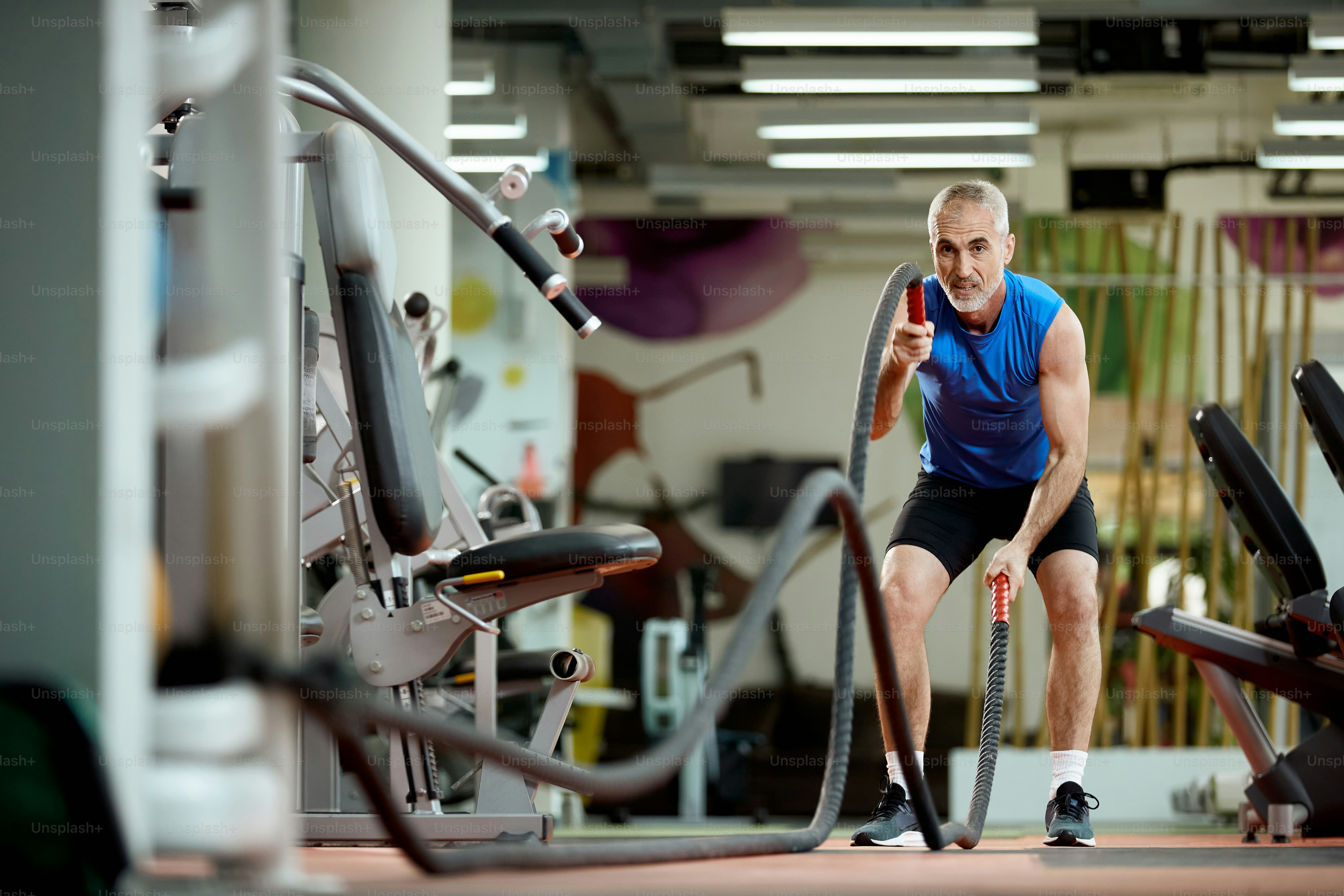 Middle aged sportsman using battle ropes during cross training in a gym.