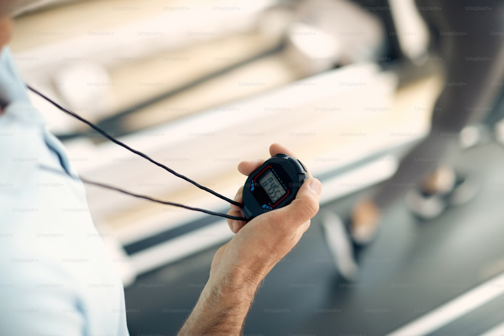 Gros plan d’un instructeur de fitness mesurant le temps sur un chronomètre lors d’un entraînement sportif dans une salle de sport.