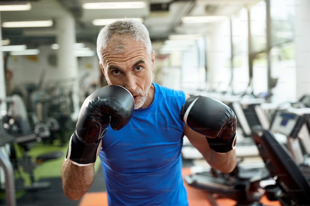 Atleta de mediana edad practicando boxeo mientras hace ejercicio en un gimnasio y mira a la cámara.