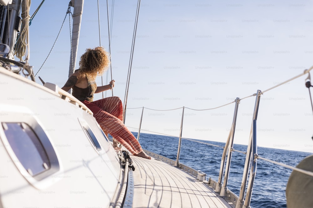 One woman sit down on sail boat deck enjoy the sea travel alone and enjoy outdoor ocean leisure activity - summer holidays excursions and trip female people - blue sky in background