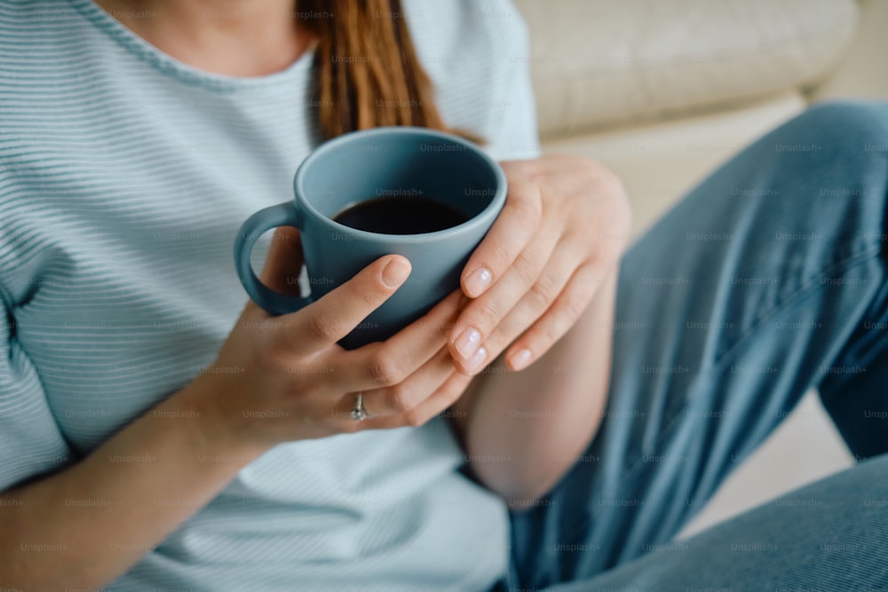 Mujer irreconocible bebiendo café mientras se relaja en el sofá de su casa.