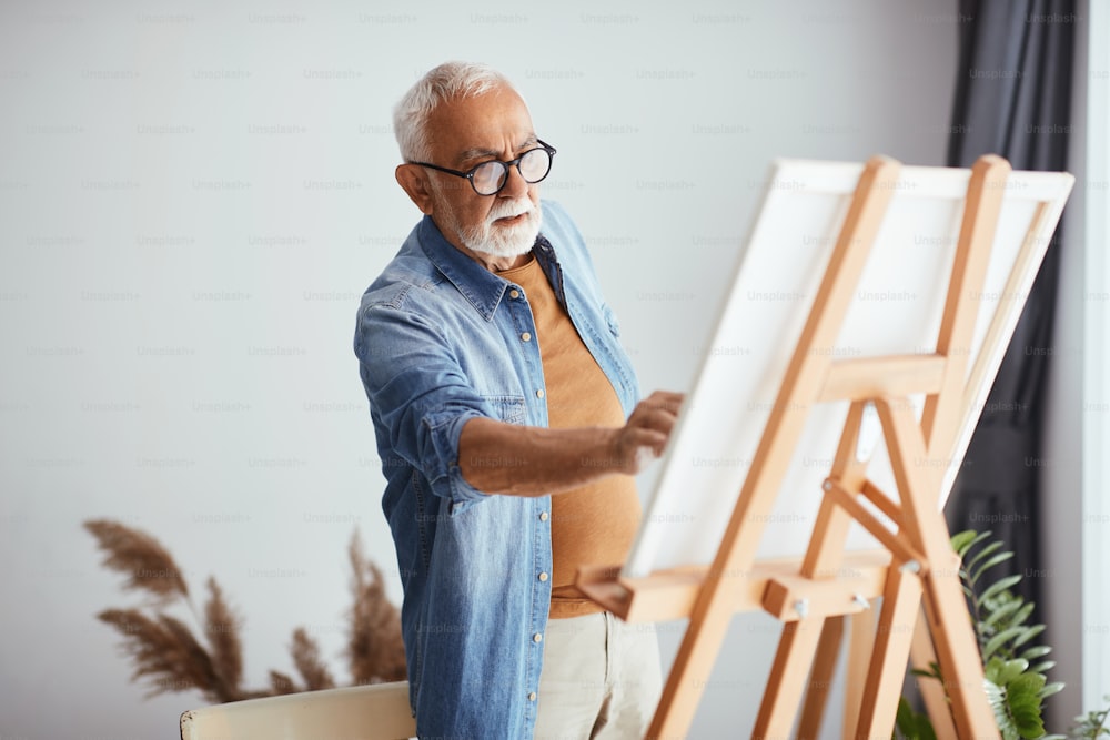 Uomo anziano creativo che si diverte mentre dipinge su tela a casa.