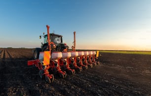 Farmer with tractor seeding - sowing crops at agricultural field. Plants, wheat.