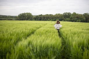 Woman with big white sheepdog running on green rye field. Farming and countryside life. Freedom and activity. Copy space. Rear view