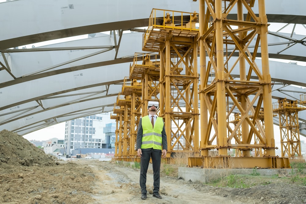 Young builder in formalwear and vr headset standing on construction site