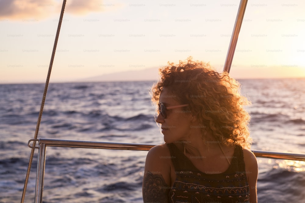 Beautiful woman enjoy the sunset sitting on the yacht in sea trip tour travel - happy female people portrait in outdoor with sunset  colors and ocean in background