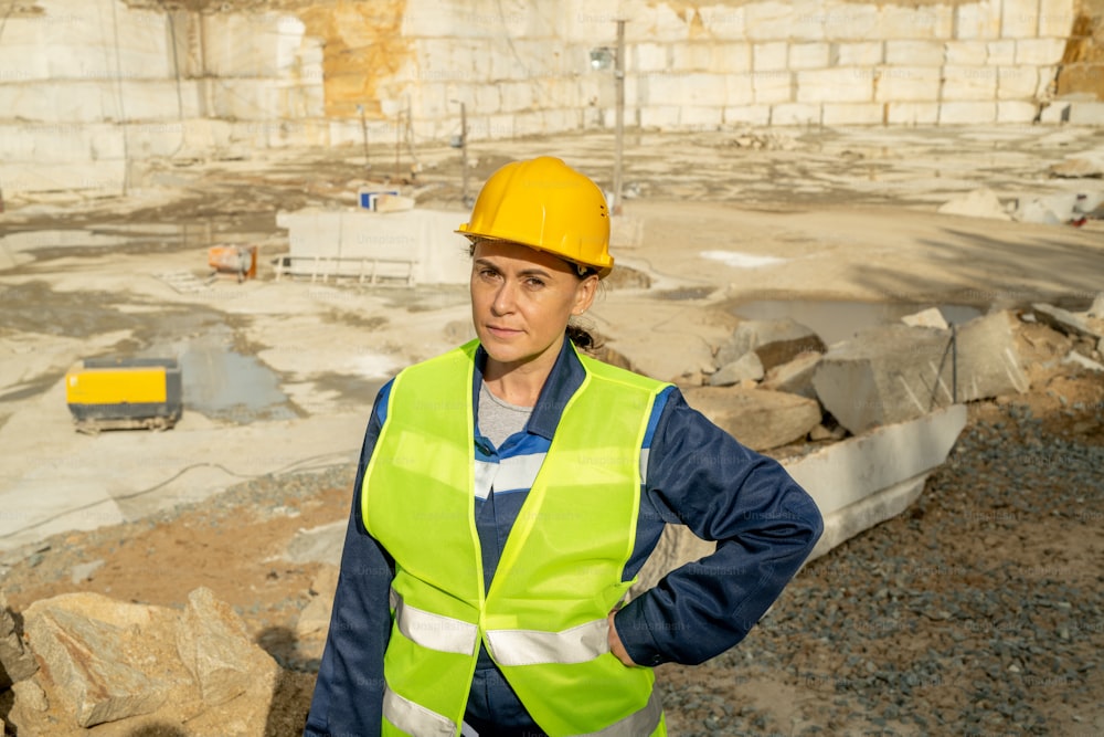 Costruttore femminile maturo in abbigliamento da lavoro che ti guarda sul sito di costruzione