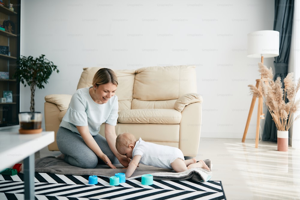 Junge Mutter hat Spaß mit ihrem kleinen Sohn, während sie mit ihm auf dem Boden im Wohnzimmer spielt.