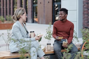 Two young multiracial co-workers having lunch on bench outdoors