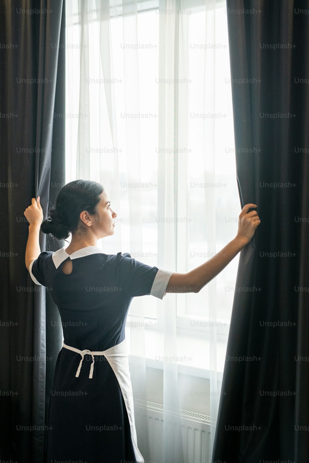Jeune femme de chambre debout près de la fenêtre dans la chambre d’hôtel