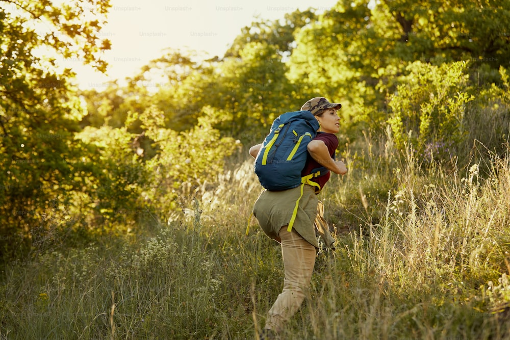 Young woman carrying backpack and climbing up while hiking in nature.