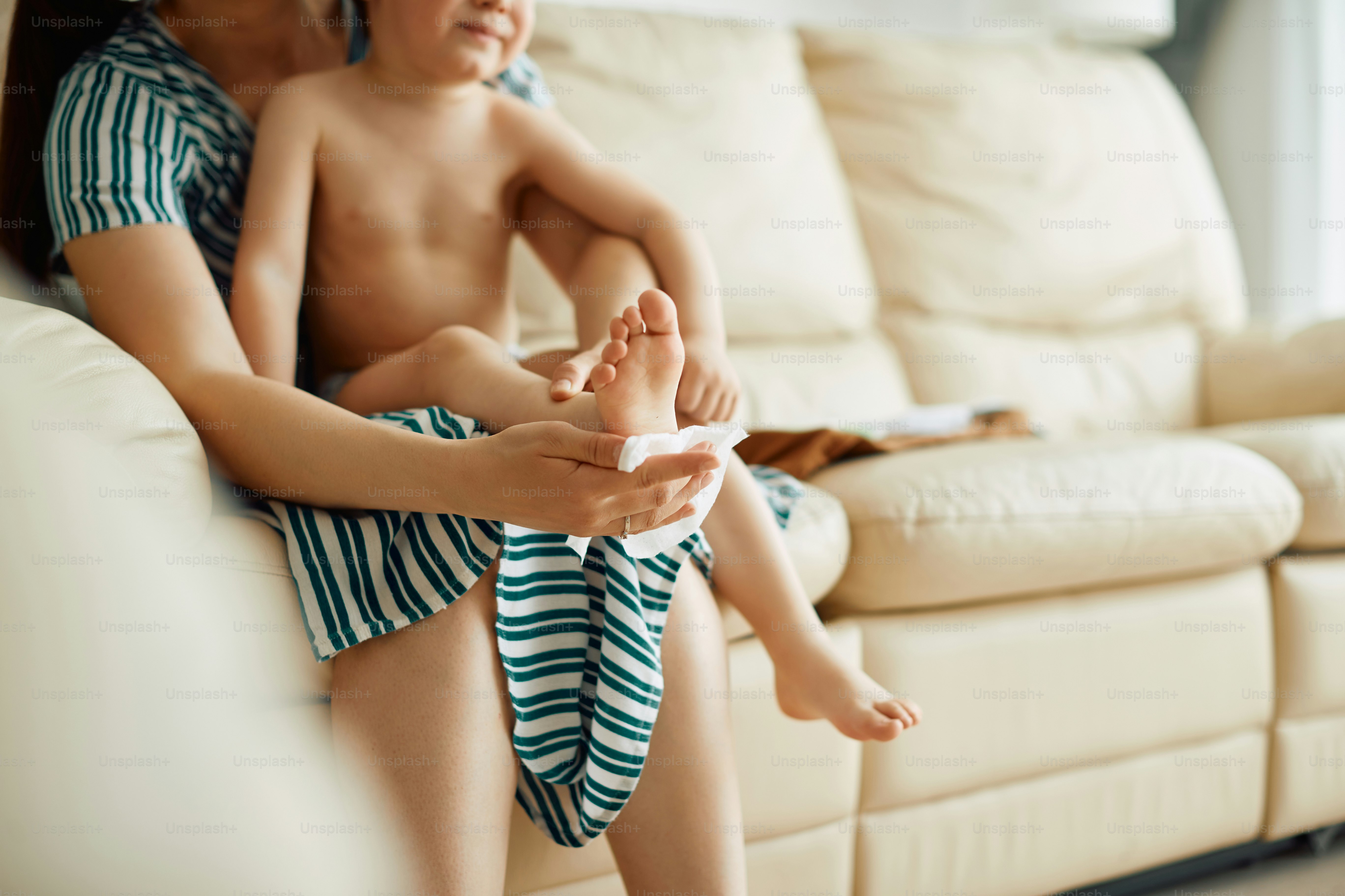 Une mère méconnaissable essuie les pieds de son fils avec un mouchoir à la maison.
