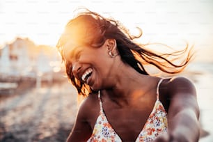 Mulher alegre sorrindo na praia ao pôr do sol - Mulher africana feliz se divertindo andando à beira-mar - Pessoas e conceito de felicidade