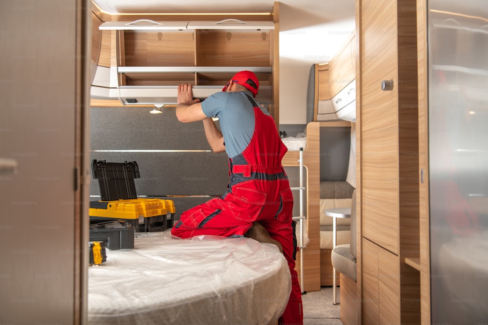 Caucasian RV Campers Technician in His 40s Performing Repairs Inside Modern Travel Trailer. Recreational Vehicles Maintenance.