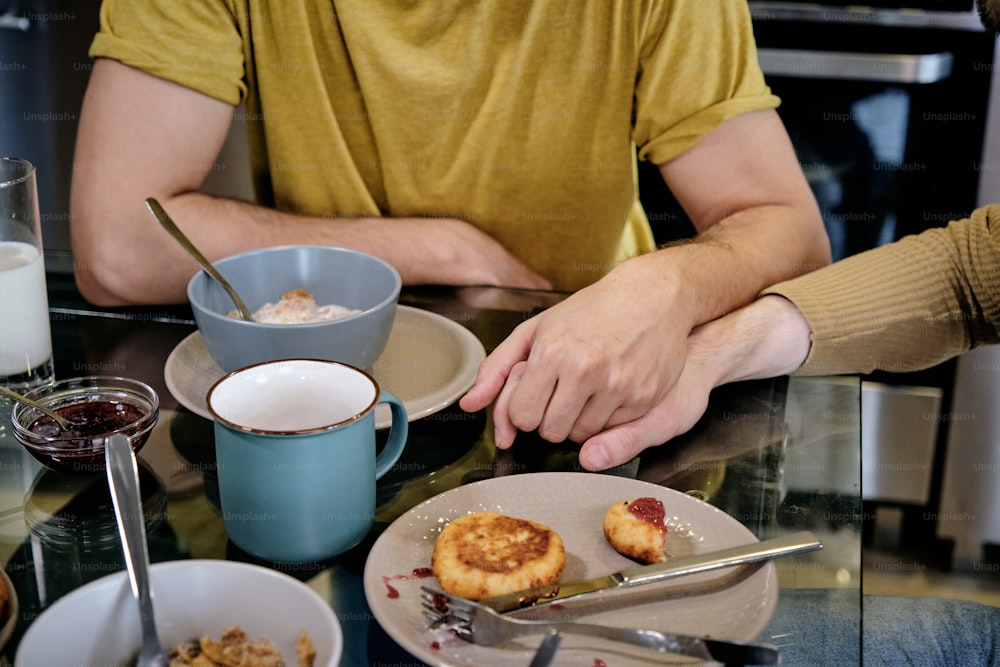 Two guys holding hands when eating breakfast together at home