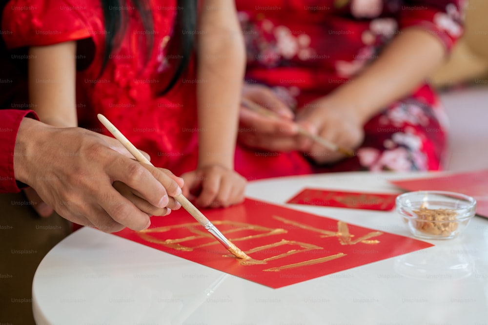 Hands of young Chinese man and his little daughter painting new year postcard