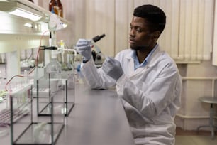 Young African male scientist taking new vaccine into syringe before making injection