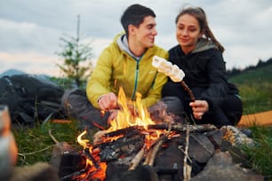 Classical marshmallow making near campfire. Young couple. Majestic Carpathian Mountains. Beautiful landscape of untouched nature.