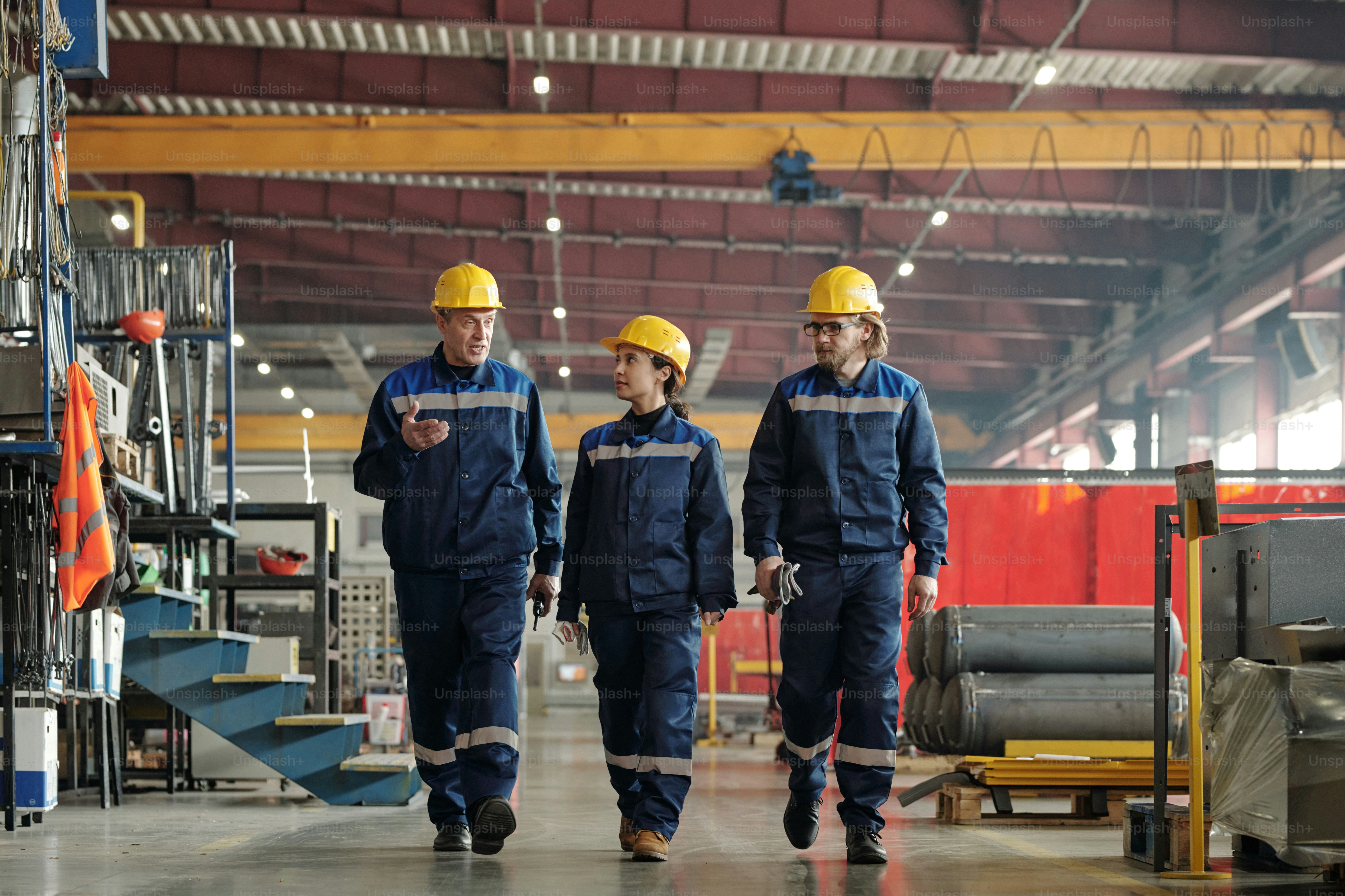 Capataz de fábrica maduro andando ao longo da oficina e gesticulando a mão enquanto explica as tarefas aos funcionários da indústria