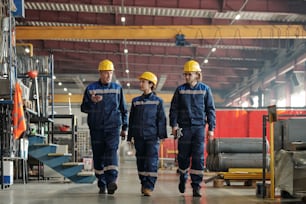 Mature factory foreman walking along workshop and gesturing hand while explaining tasks to employees in industry
