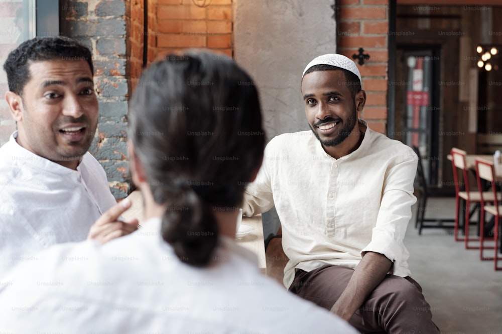 Grupo de hombres negros islámicos sentados en una cafetería y discutiendo noticias mientras pasan tiempo juntos