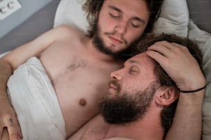 Tender portrait of male couple in bed together. Two bearded long haired man hugging, cuddling in bed. Gay couple, relationship, diversity concept