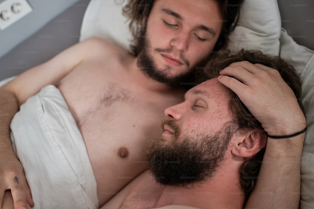 Retrato terno do casal masculino na cama juntos. Dois homens barbudos de cabelos compridos se abraçando, abraçados na cama. Casal gay, relacionamento, conceito de diversidade
