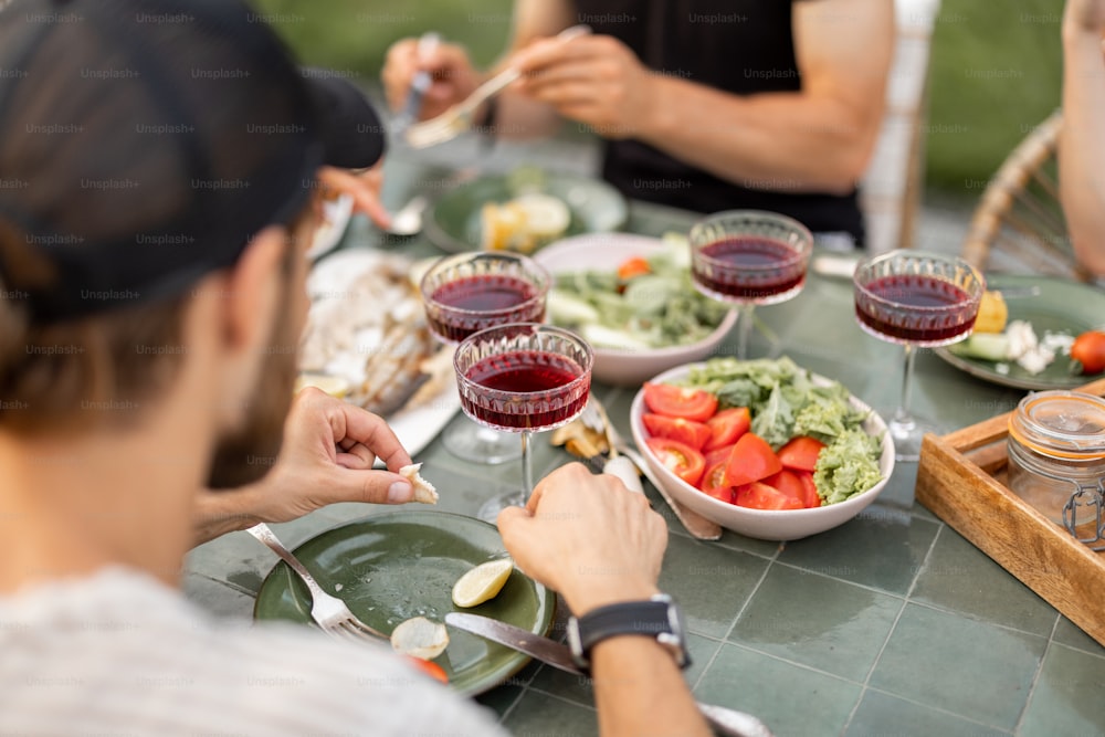 Small group of a young friends have a lunch outdoors, eating grilled vegetables and fish and having fun at backyard