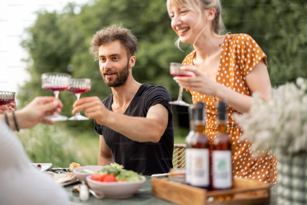 Junge Freunde essen festlich im Freien, stoßen an und trinken Wein, verbringen glückliche Sommerzeit zusammen