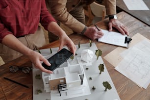 Directly above view of unrecognizable assistant photographing 3D model of house while architect making notes about room space