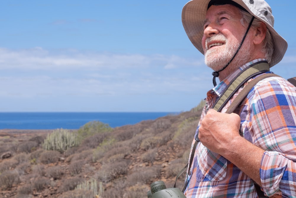 Viaggiatore anziano che si gode l'escursione all'aperto camminando tra montagna e mare, indossando berretto e zaino