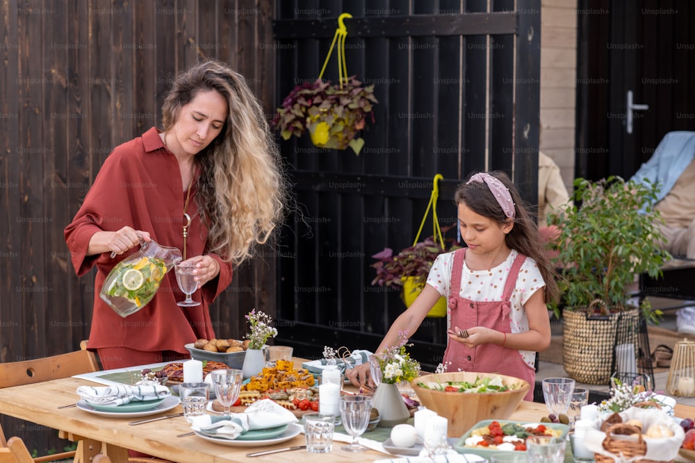 Preteen girl helping mother to serve dinner table for party or other event in backyard
