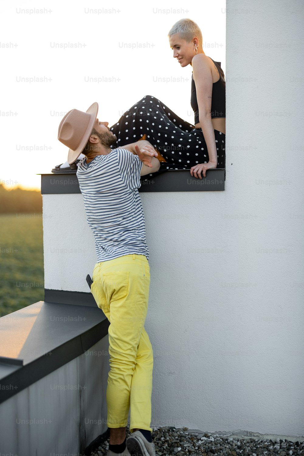 La coppia elegante ha una conversazione ravvicinata mentre è seduta sul tetto con una splendida vista sul tramonto sulla natura. Stile di vita spensierato e concetto di romanticismo