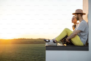 Stylish couple have a close conversation while sitting together on the rooftop with great sunset view on nature. Carefree lifestyle and romance concept