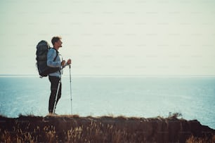 The traveler with backpack standing on the mountain top above the sea