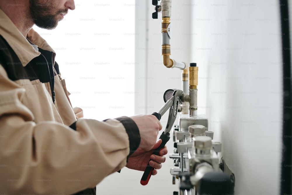 Repairman with wrench fixing parts of pipes in modern flat