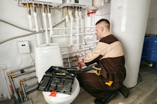 Young male worker in uniform repairing pipes in lavatory