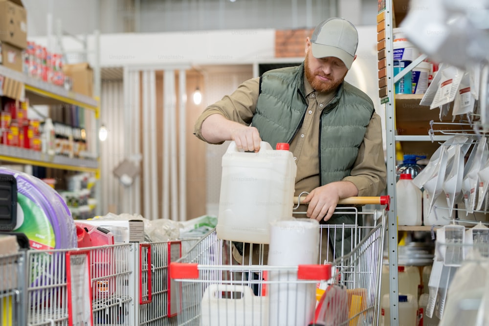 Bearded customer putting household goods into shopping cart in hardware store