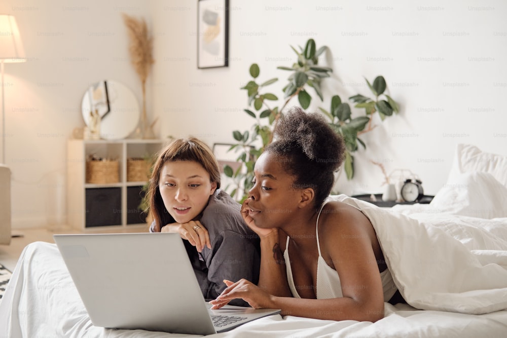 Dos chicas desplazándose a través de videos en línea en una computadora portátil mientras eligen algo para ver