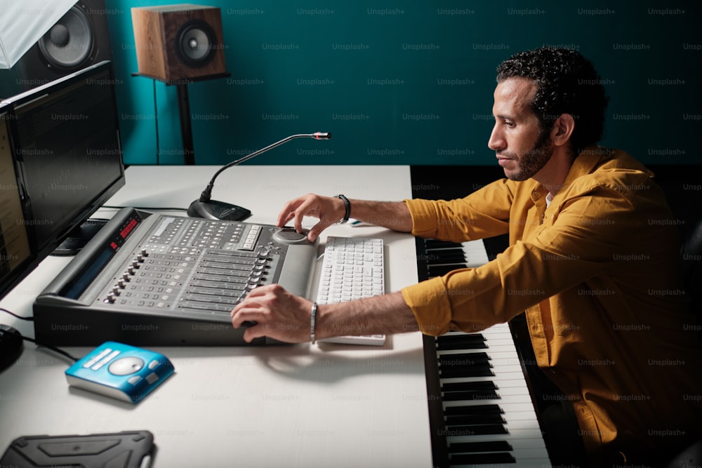 Portrait of moroccan man in yellow shirt using stage mixer controller in professional recording studio