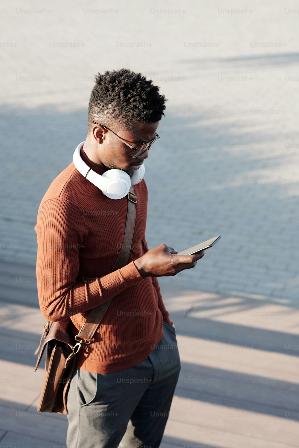 Young African businessman in smart casualwear scrolling in smartphone after work on summer day